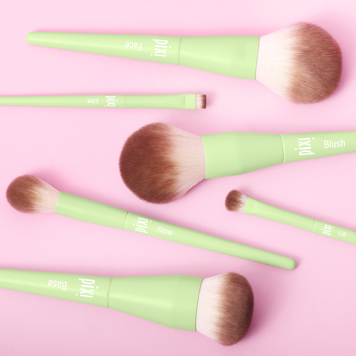 Set of Pixi makeup brushes with green handles on a pink background
