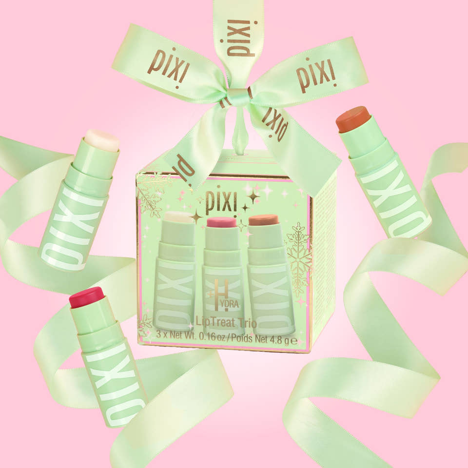 Pixi+Hydra LipTreat Trio gift set in a clear window box, wrapped in a mint green ribbon printed with the Pixi+ brand name, set against a solid pink background. view 2