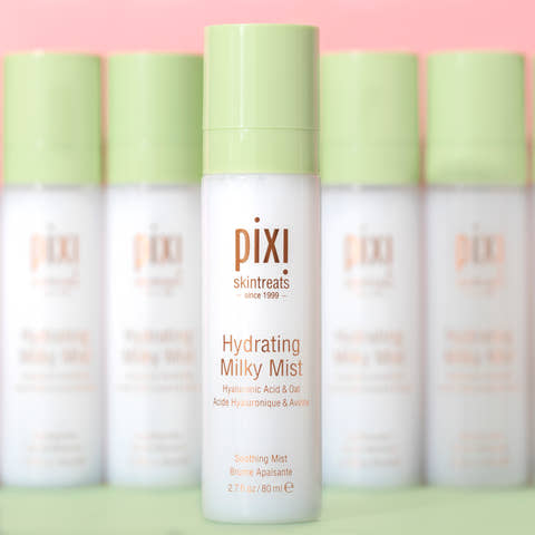 Row of Pixi skincare hydrating milky mist bottles on a pink background with shallow focus